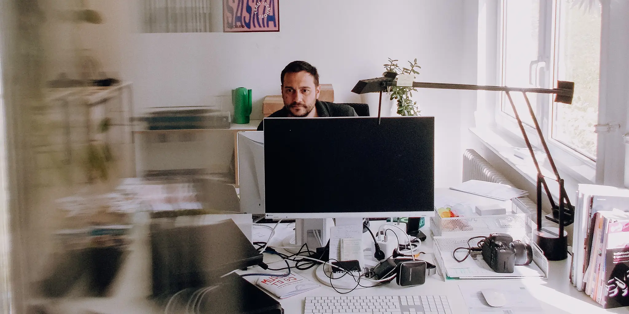Andreas, der an seinem Schreibtisch neben einem Fenster in der Isenhoff Agentur in Kempten sitzt und konzentriert in seinen Computermonitor schaut.
